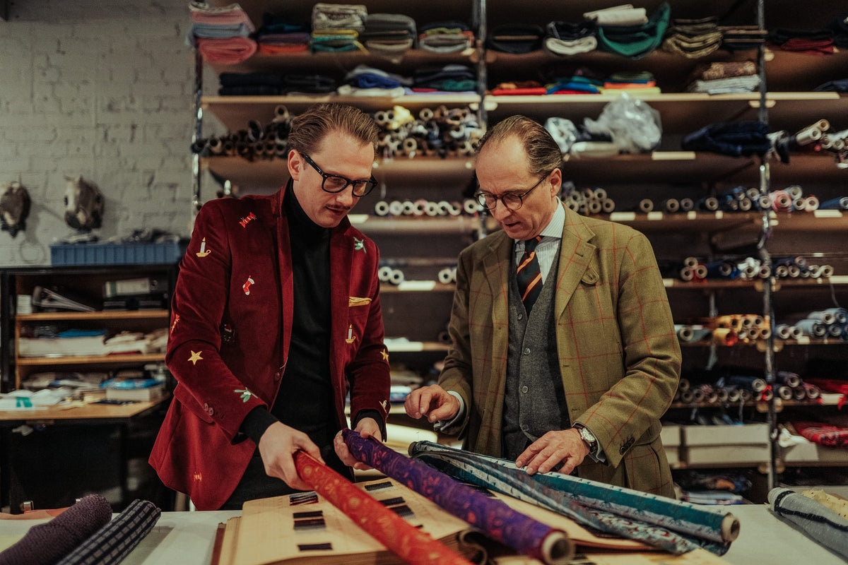 Jan-Henrik M. Scheper-Stuke und ein Kunde im Tweed rollen vor dem Stoffregal Seidenballen aus